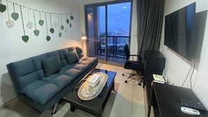 A modern living room with a sofa, coffee table, TV, and a balcony with a city view. - Unixx condo (Pattaya)