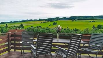 Een terras met metalen stoelen en een tafel, uitkijkend op een groen landschap met velden en bomen.