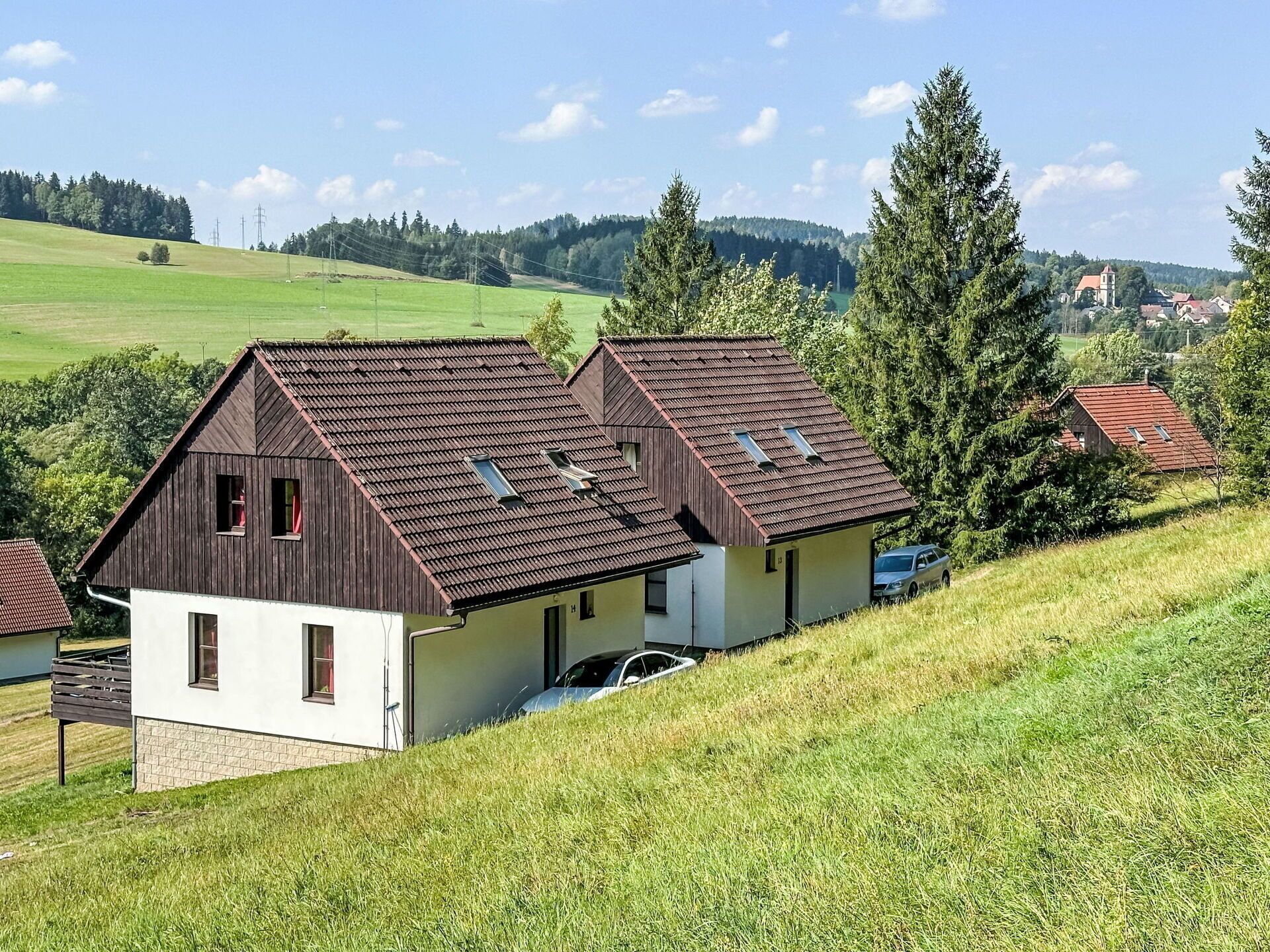 Une maison à deux étages avec un toit en pente, une voiture garée dans l’allée et un grand arbre au premier plan.