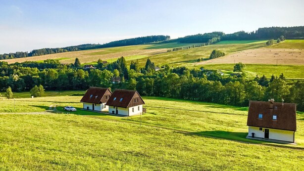 A rural landscape with two white houses with brown roofs, surrounded by green fields and trees.