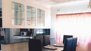 Un comedor con mesa y sillas, una cocina con microondas y un ventanal con cortinas.