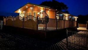 A wooden cabin with a covered porch, a fenced deck, and a brick wall. - Relax at our Lodge in the Cheshire Countryside (Congleton)