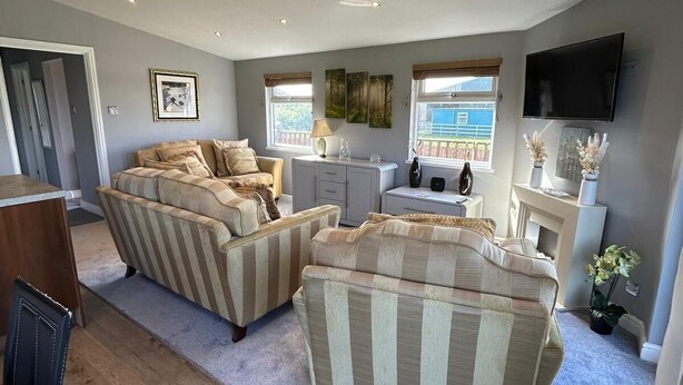 A spacious living room with a large sofa set, a flat-screen TV mounted on the wall, and a fireplace. - Relax at our Lodge in the Cheshire Countryside (Congleton)