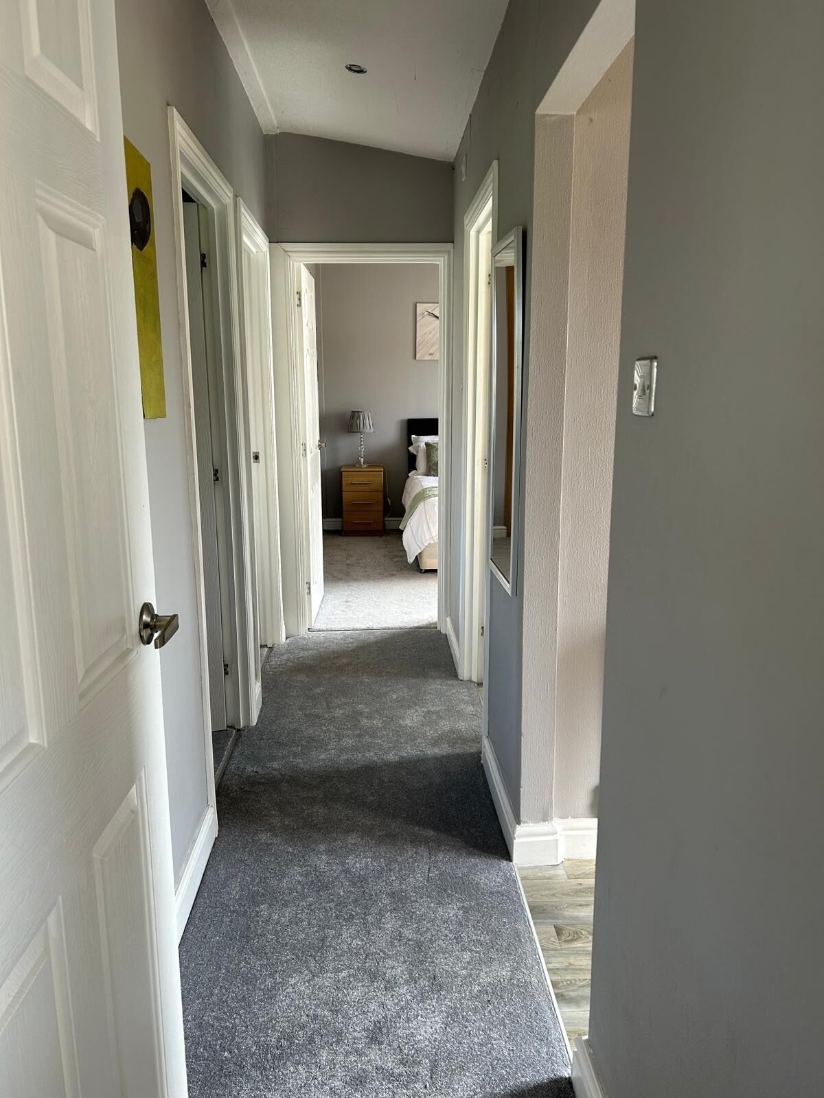 A hallway leading to a bedroom with a bed, dresser, and lamp.