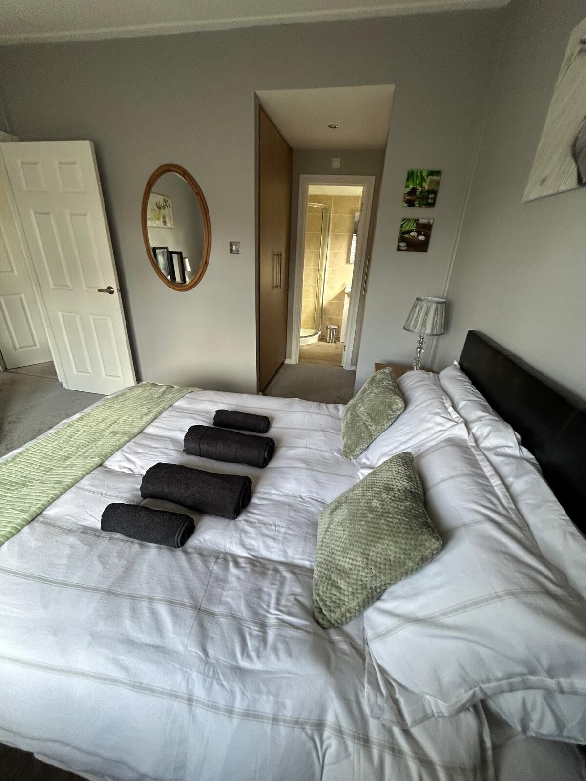 A neatly made bed with pillows and rolled towels, a bedside lamp, and a mirror on the wall.