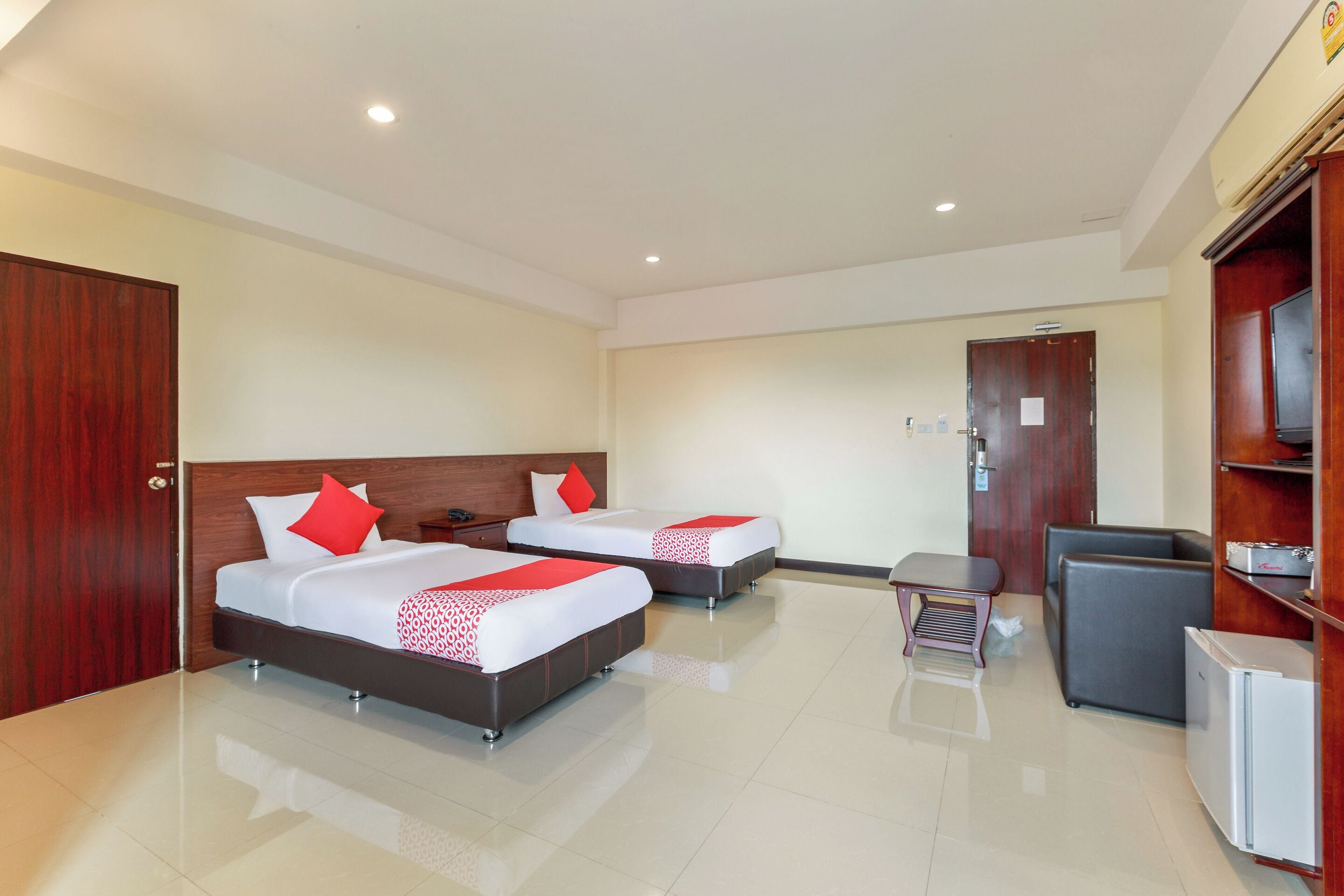 A hotel room with two beds, a desk, a chair, a TV, and a minibar.