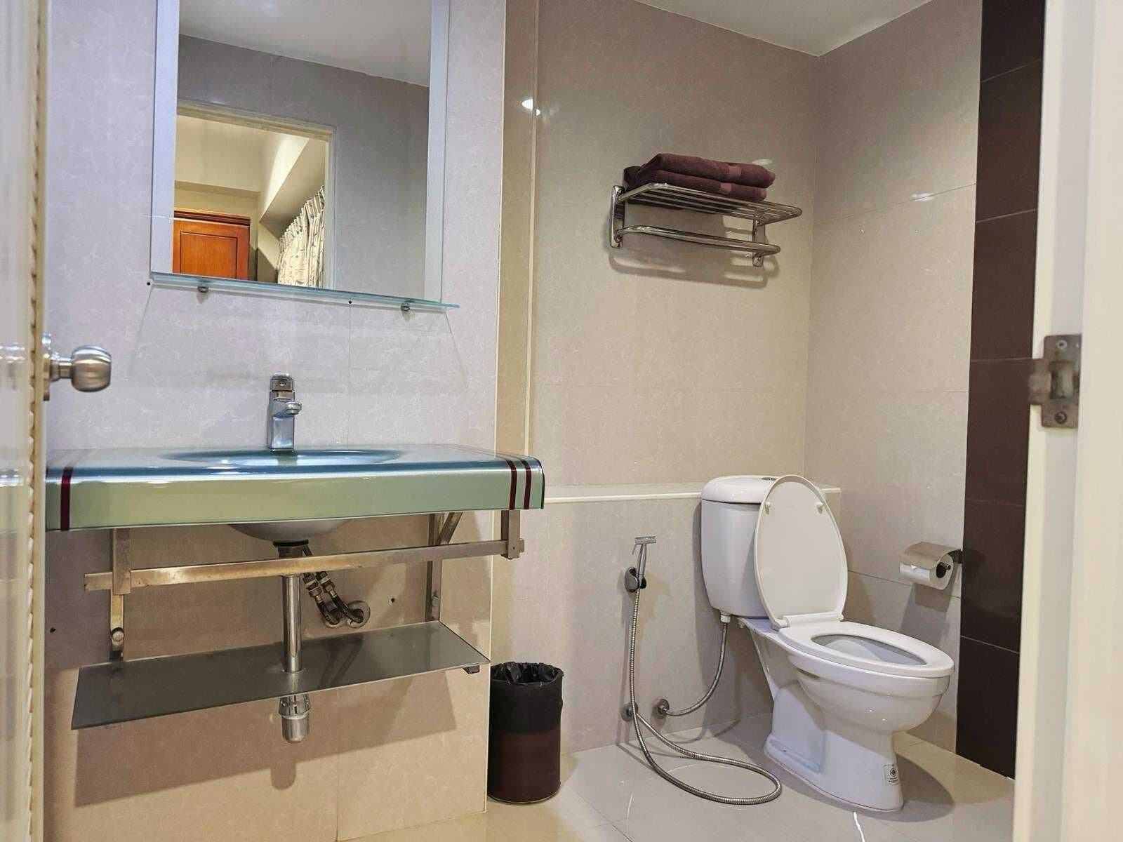 A bathroom with a glass sink, a toilet, a trash bin, and a towel rack.