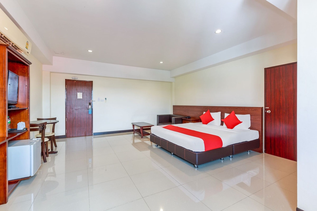 A hotel room with a bed, bedside table, a small desk with a chair, a TV, and a wardrobe.
