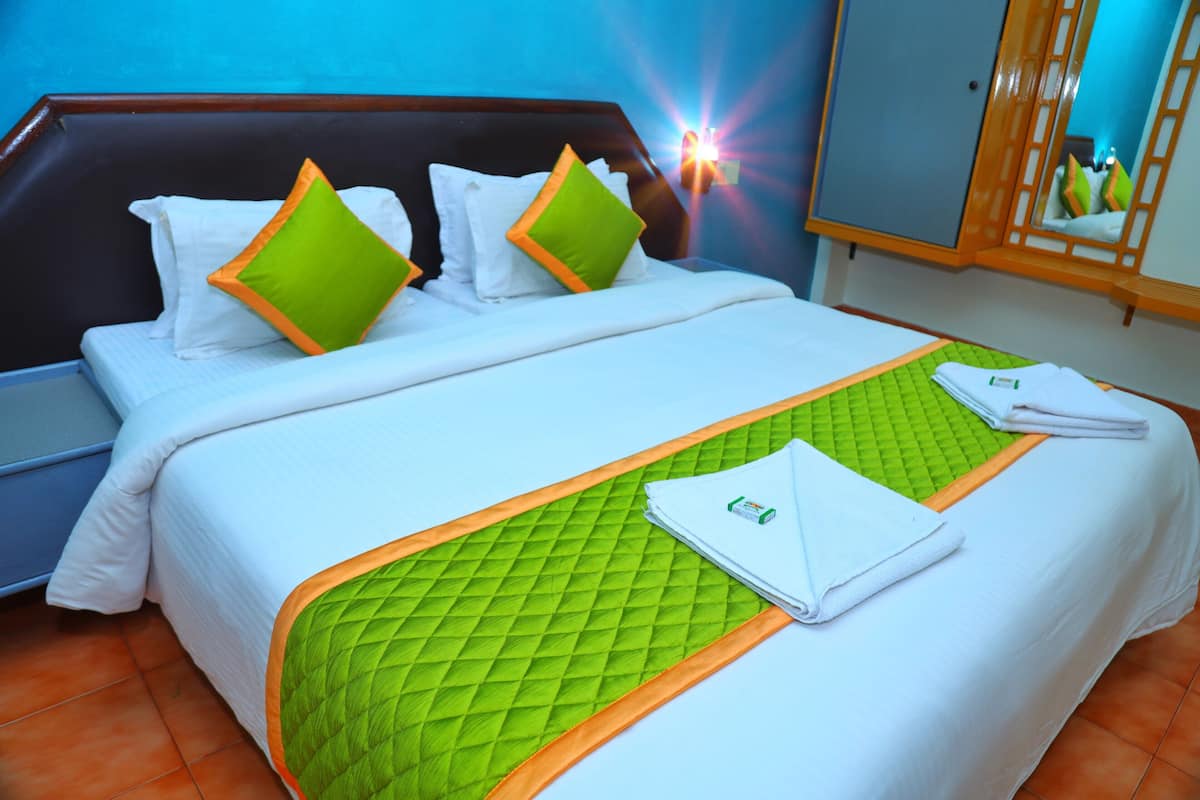 A neatly made bed with white bedding and green accents, a green quilted mat, and a folded towel on the bed.