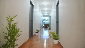 A corridor with white walls, tiled floor, and potted plants. - Grand Harmony Beach Resort (Neyyattinkara)