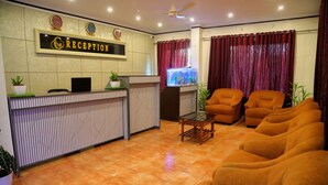 A reception area with a reception desk, a television, and a seating area with sofas. - Grand Harmony Beach Resort (Neyyattinkara)