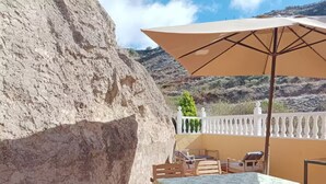 A terrace with a table and chairs, a large beige umbrella, and a view of a mountainous landscape. - House La Cabaña Galdar (Galdar)