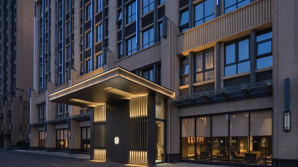 A modern hotel entrance with a covered entrance area, large windows, and a well-lit facade.