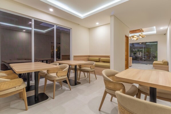 Un espace repas moderne avec des tables rondes et des chaises en osier, de grandes fenêtres et une vue sur l’extérieur.