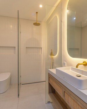 Une salle de bain moderne avec une douche à parois de verre, des toilettes blanches et un meuble-lavabo doté d’un grand miroir.