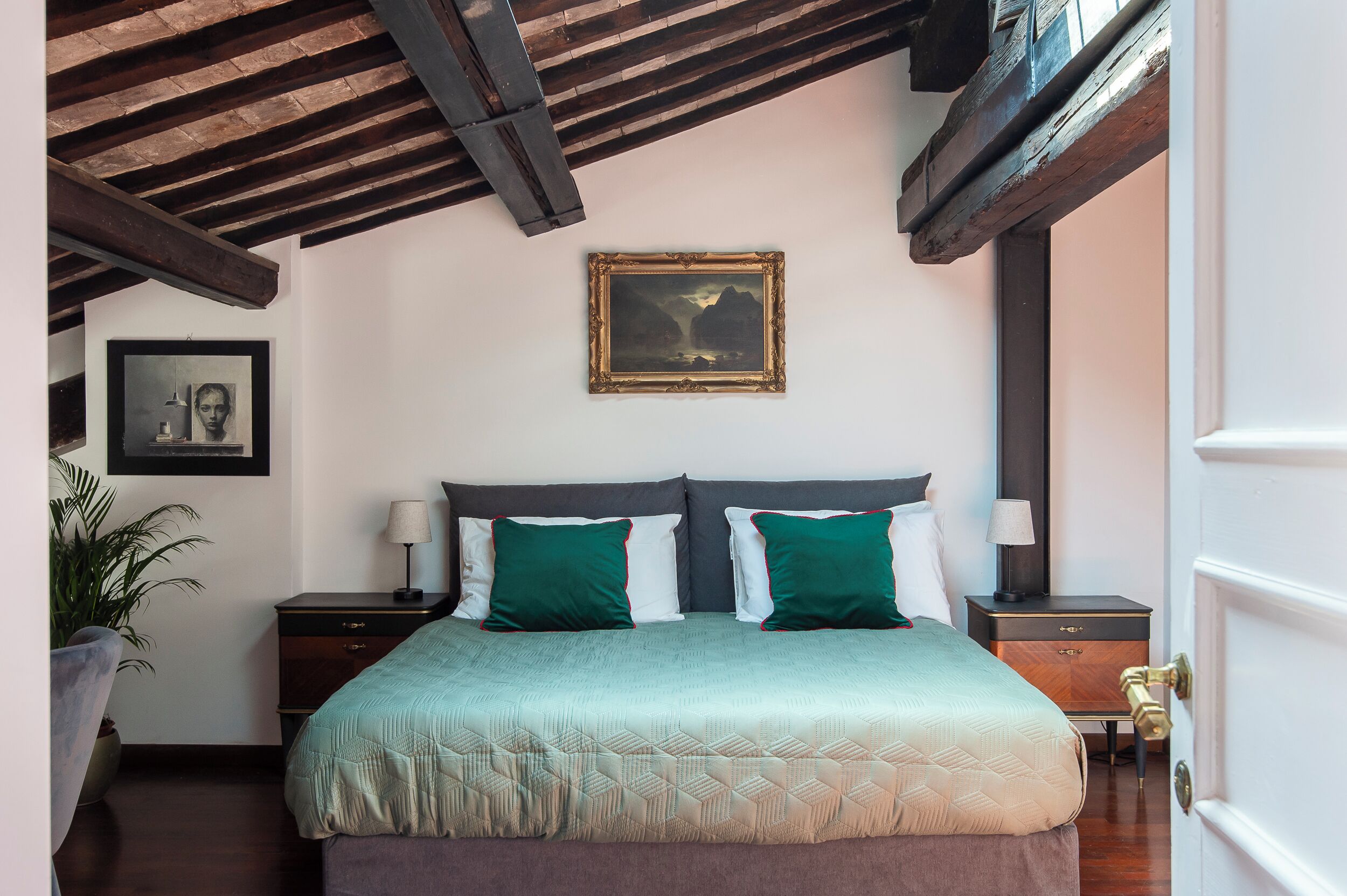Un dormitorio con una cama, dos mesitas de noche, un cuadro grande enmarcado en la pared y una planta en maceta.