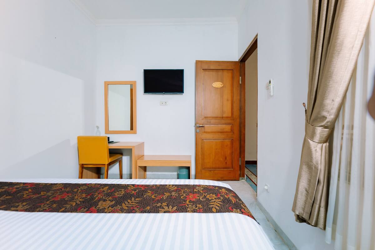 A hotel room with a bed, a desk, a chair, a television, and a door.