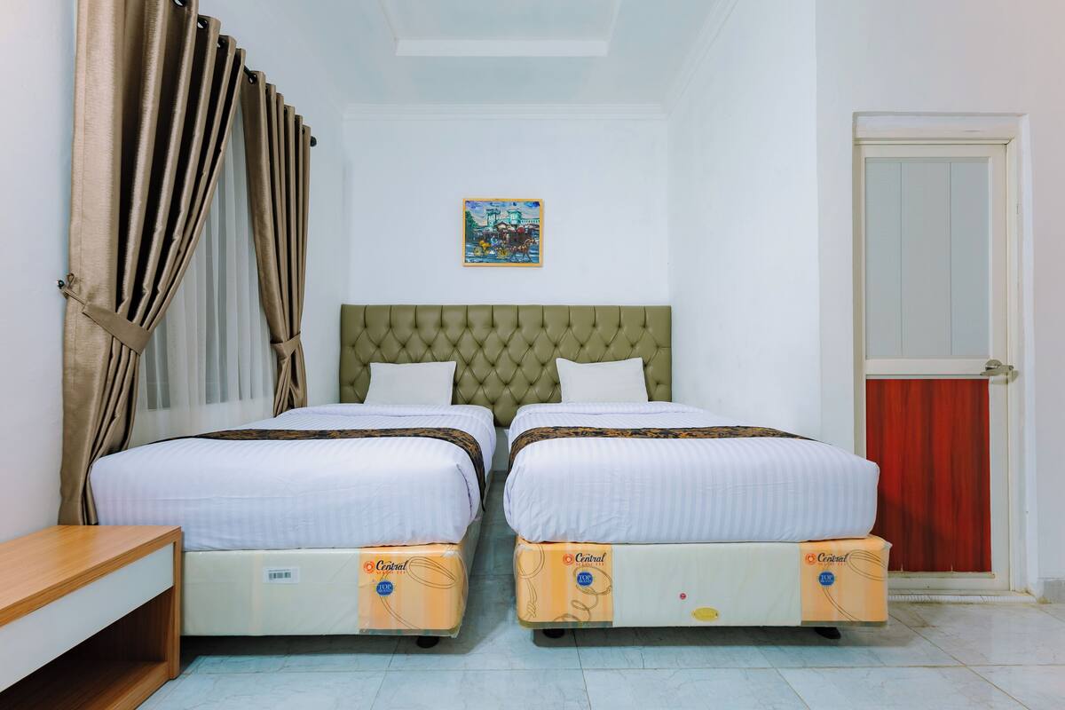 A room with two beds, a tufted headboard, a small table, and a door with a red curtain.