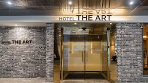 La entrada al Hotel The Art, con fachada de ladrillo y puertas de vidrio.
