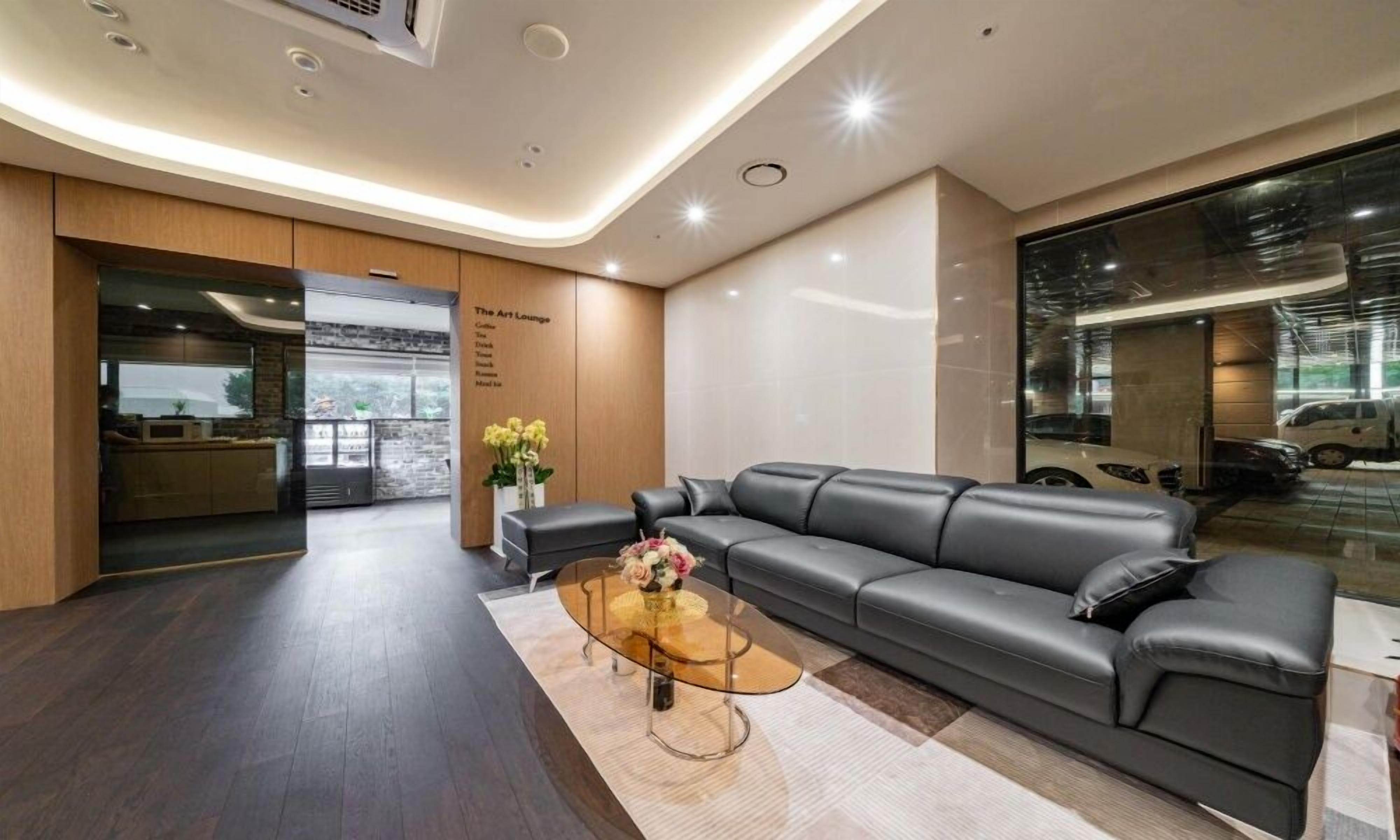 A modern lounge area with a leather sofa, a glass coffee table, and a menu board listing coffee, tea, and snacks.