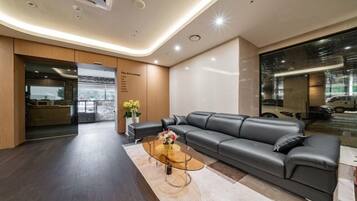 A modern lounge area with a leather sofa, a glass coffee table, and a menu board listing coffee, tea, and snacks.