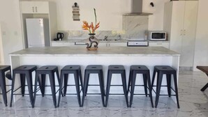 A modern kitchen with a marble countertop, a central island with stools, white cabinets, a microwave, and a stainless steel range hood. - Te Aro Villa 2
Modern Brand New 3brm villa with pool in Muri (Ngatangiia District)