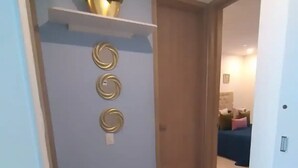 Een hal met een vloerkleed met geometrisch patroon, een wandplank met een plant, en drie ronde decoraties aan de muur.