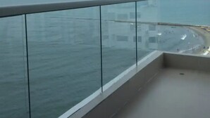 Een balkon met glazen hekwerk met uitzicht op een strand en de oceaan.