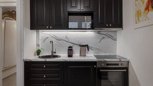 Une cuisine moderne avec des meubles de couleur sombre, un dosseret en marbre et des appareils électroménagers intégrés, notamment une machine à café et un four.