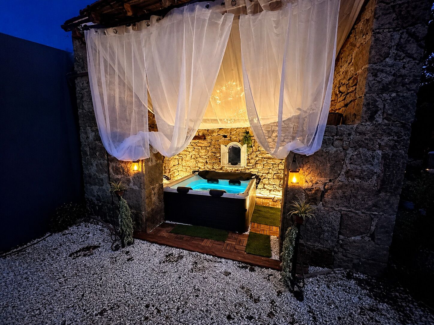 Un edificio de piedra con jacuzzi, cortinas blancas y paredes de piedra.