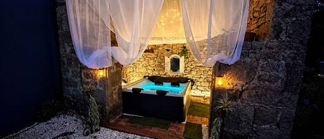 Un edificio de piedra con jacuzzi, cortinas blancas y paredes de piedra.