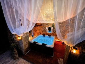 A hot tub with a stone wall backdrop, a small window, and a wooden floor. - Domaine Valenquercy (Le Vignon-en-Quercy)