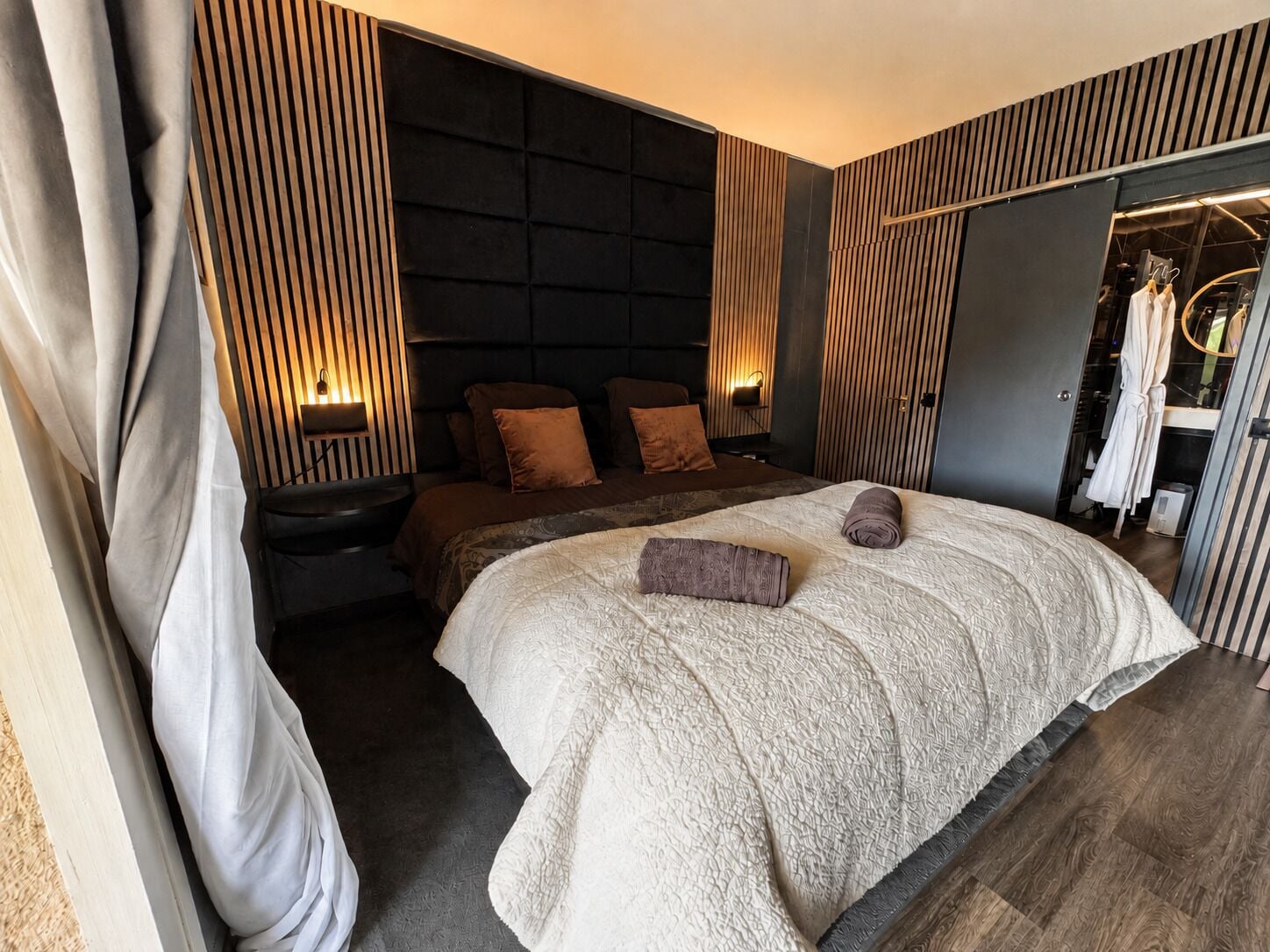 Un dormitorio moderno con una cama grande, mesitas de noche, un armario y un espejo.