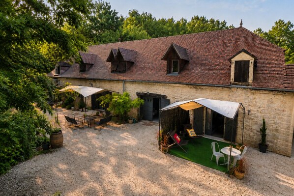 A rustic stone building with a tiled roof, outdoor seating area, and a covered space with a table and chairs. - Domaine Valenquercy (Le Vignon-en-Quercy)