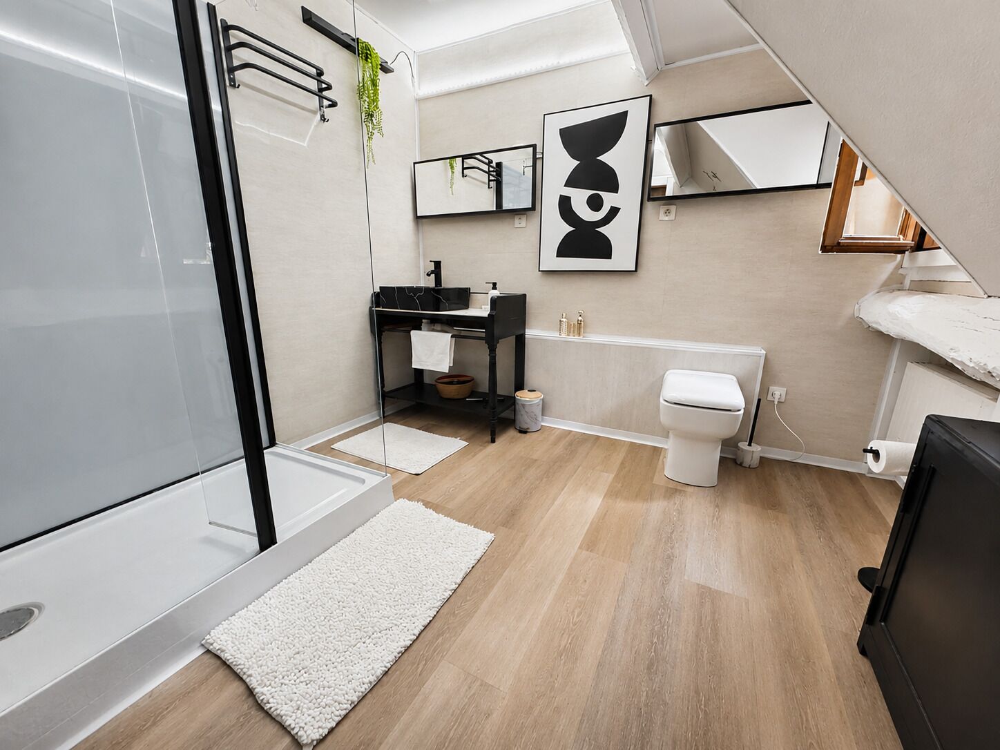 Un baño moderno con cabina de ducha de vidrio, tocador negro, inodoro blanco y un espejo grande.