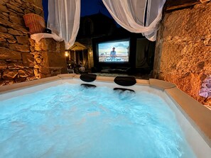 Un bain à remous avec des murs en pierre et un écran de télévision diffusant une scÚne de plage.