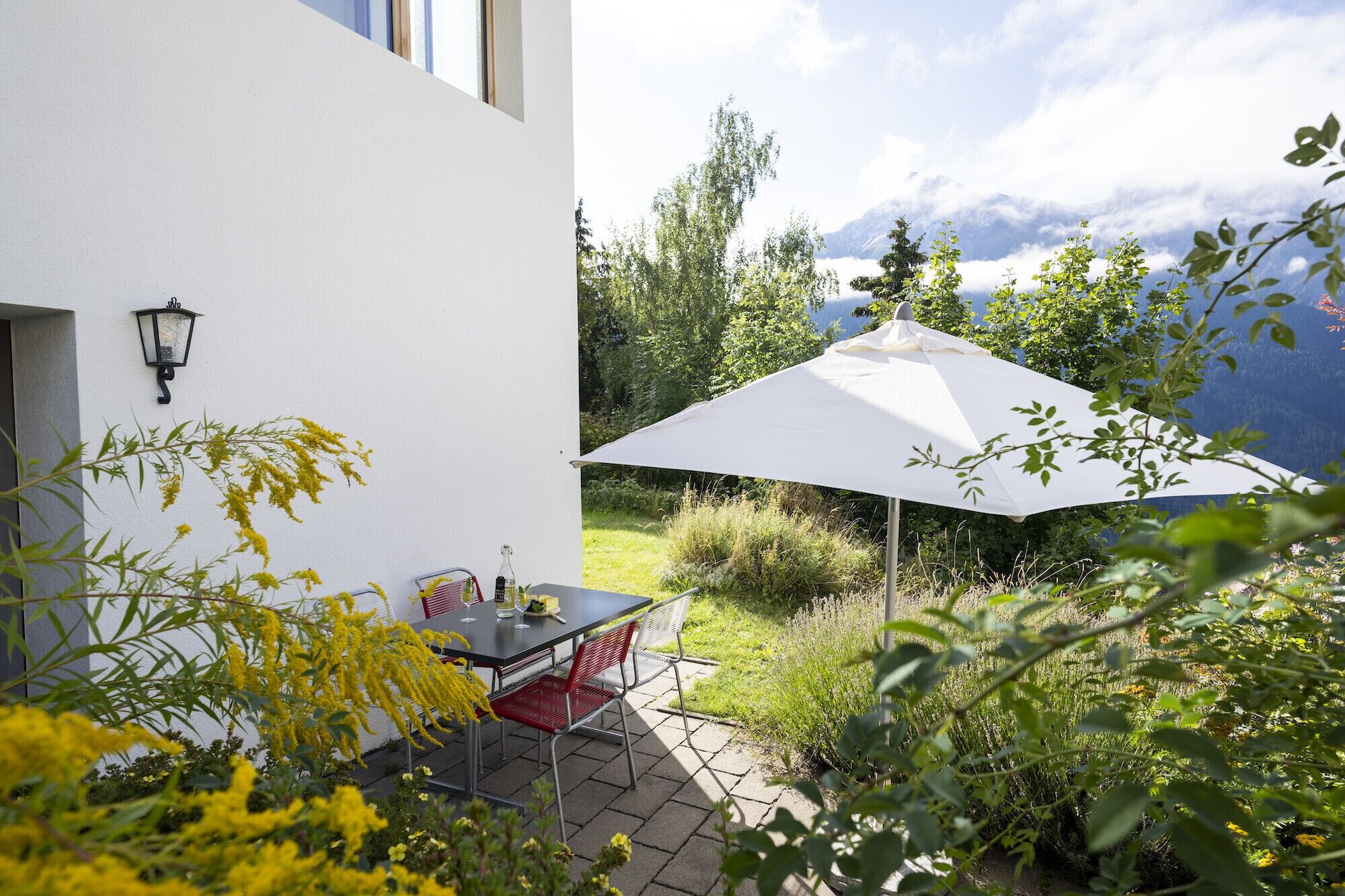 Un patio con una mesa y sillas, una sombrilla blanca y vistas a la montaña.