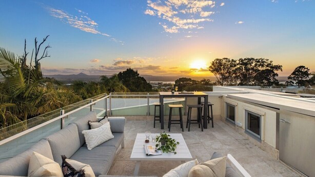 A rooftop terrace with a sofa, table, and chairs, overlooking a scenic sunset view. - White Cove Retreat, Noosa Heads (Noosa Heads)