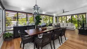 A spacious living area with a wooden dining table, wicker chairs, a sofa, and a ceiling fan. - White Cove Retreat, Noosa Heads (Noosa Heads)