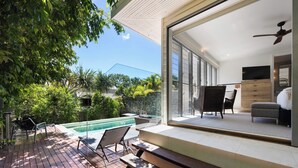 A modern outdoor living area with a pool, wooden deck, and a glass door leading to a furnished interior. - White Cove Retreat, Noosa Heads (Noosa Heads)