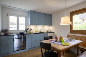 Une cuisine moderne avec des meubles gris, une table à manger en bois et une fenêtre donnant sur un paysage verdoyant.