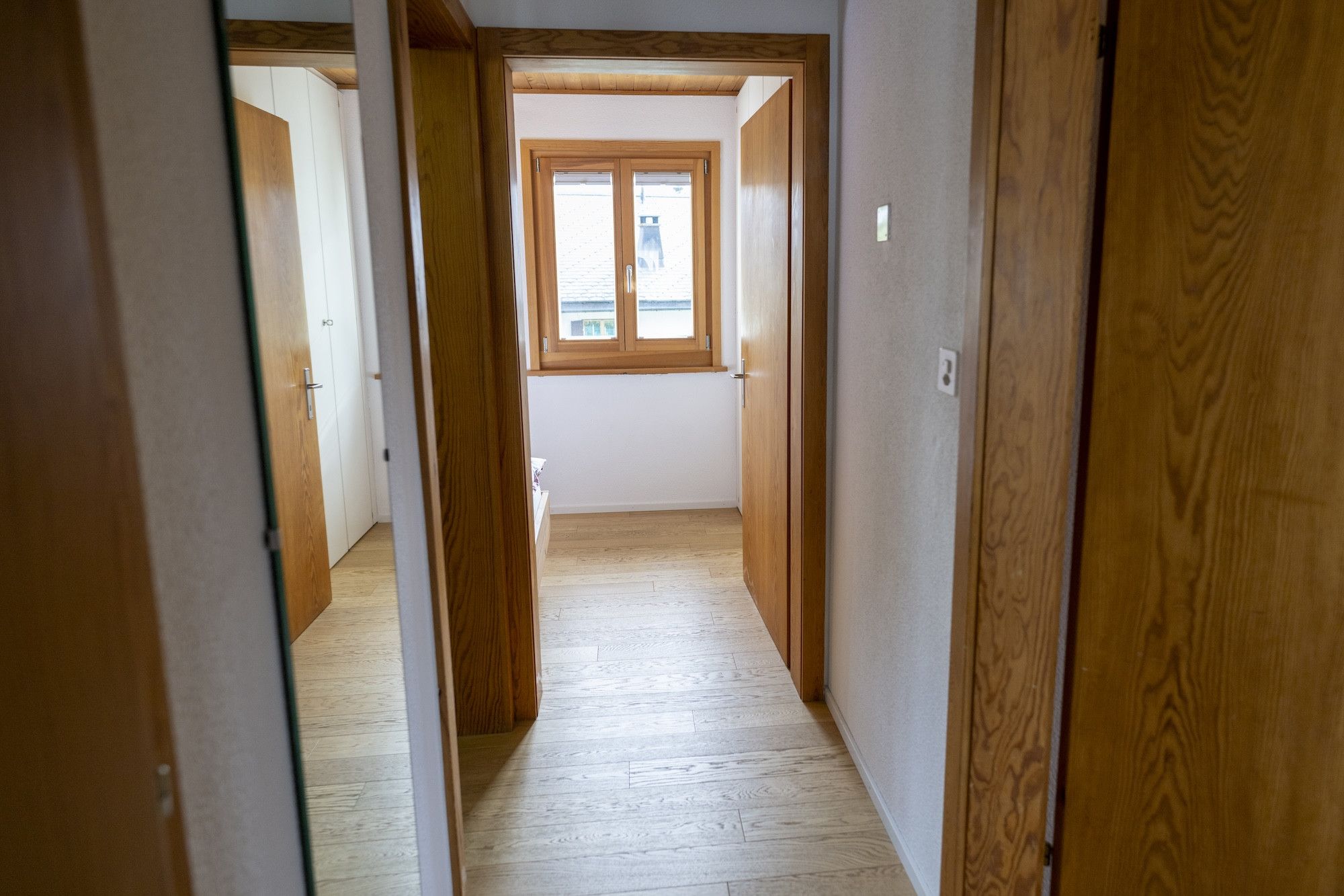 Un couloir étroit, avec des portes en bois et une fenêtre au fond.