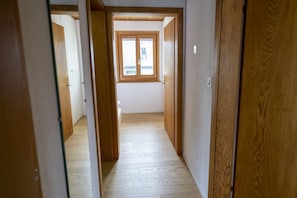Un couloir étroit, avec des portes en bois et une fenêtre au fond.
