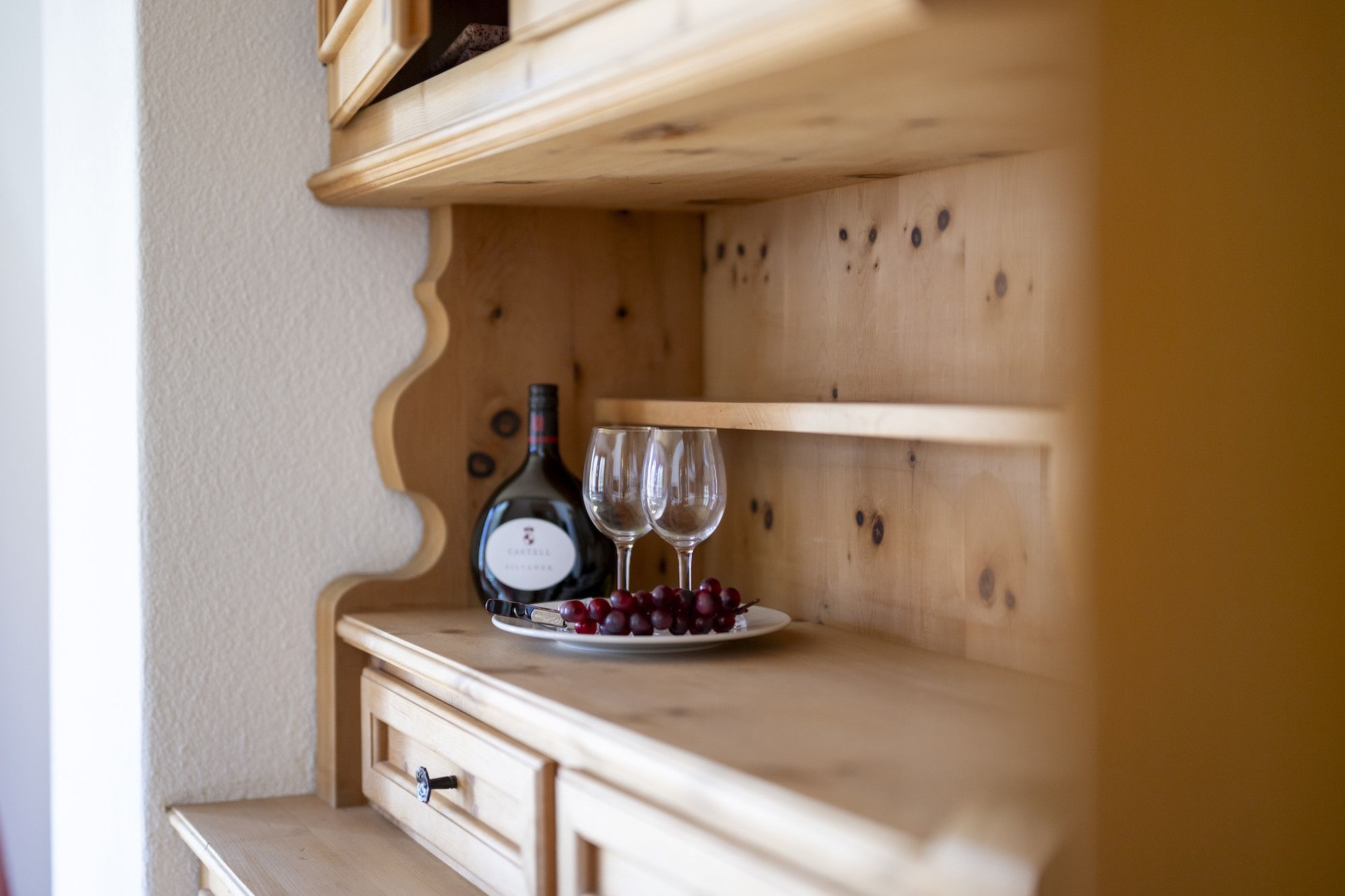 Een houten kastje met een wijnfles en twee glazen op een bord met druiven.