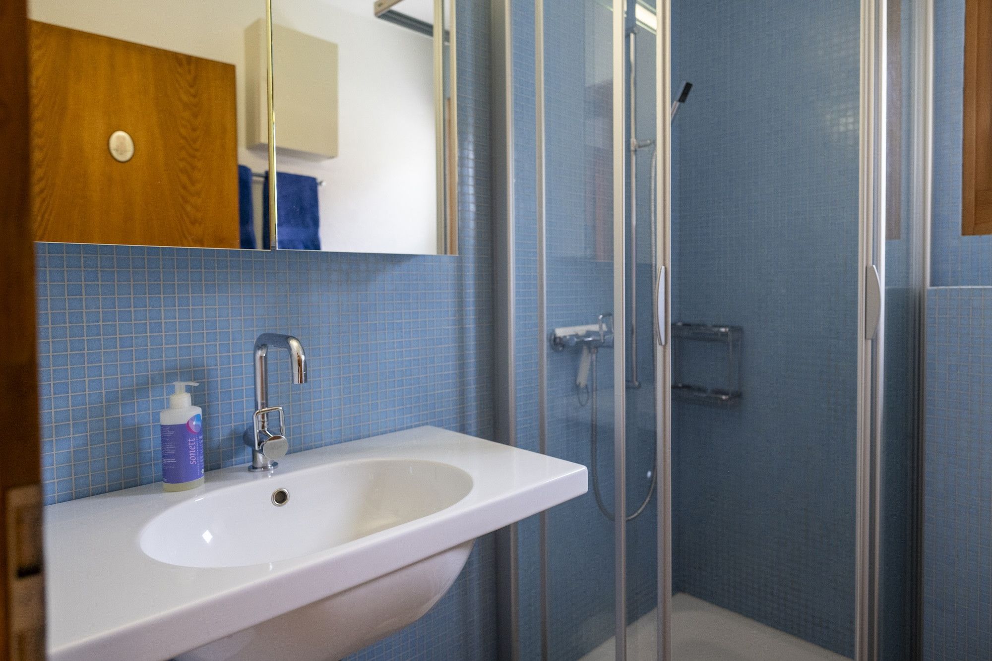 Un baño con lavamanos blanco, un espejo y una cabina de ducha con paredes de vidrio.