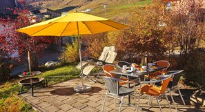 Un patio al aire libre con una mesa y sillas, un paraguas amarillo y una vista panorámica de colinas y casas.