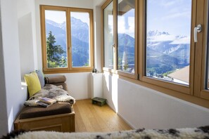Een gezellige kamer met een houten bankje, een klein tafeltje en uitzicht op met sneeuw bedekte bergen door grote ramen.