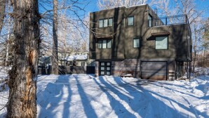 Un bâtiment à deux étages avec un garage, entouré de neige et d’arbres.