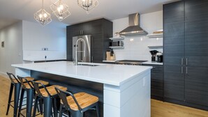 Une cuisine moderne dotée d’un grand îlot central, d’appareils électroménagers en acier inoxydable et de tabourets de bar.