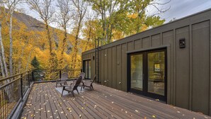 Une terrasse en bois, agrémentée de chaises et d’une table, qui offre une vue sur une zone boisée aux couleurs automnales.